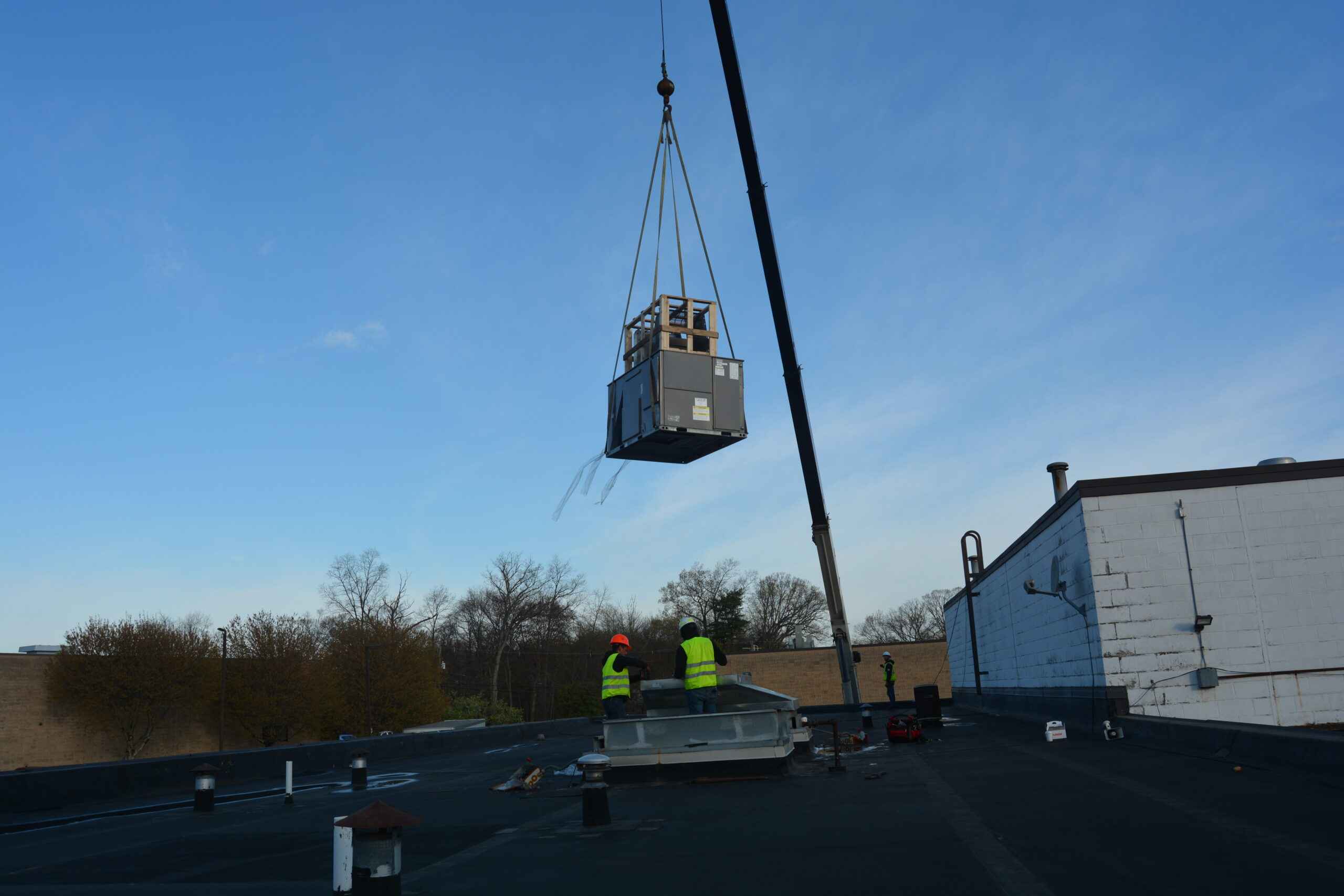 Crane lifting a rooftop HVAC unit into place on a commercial roof