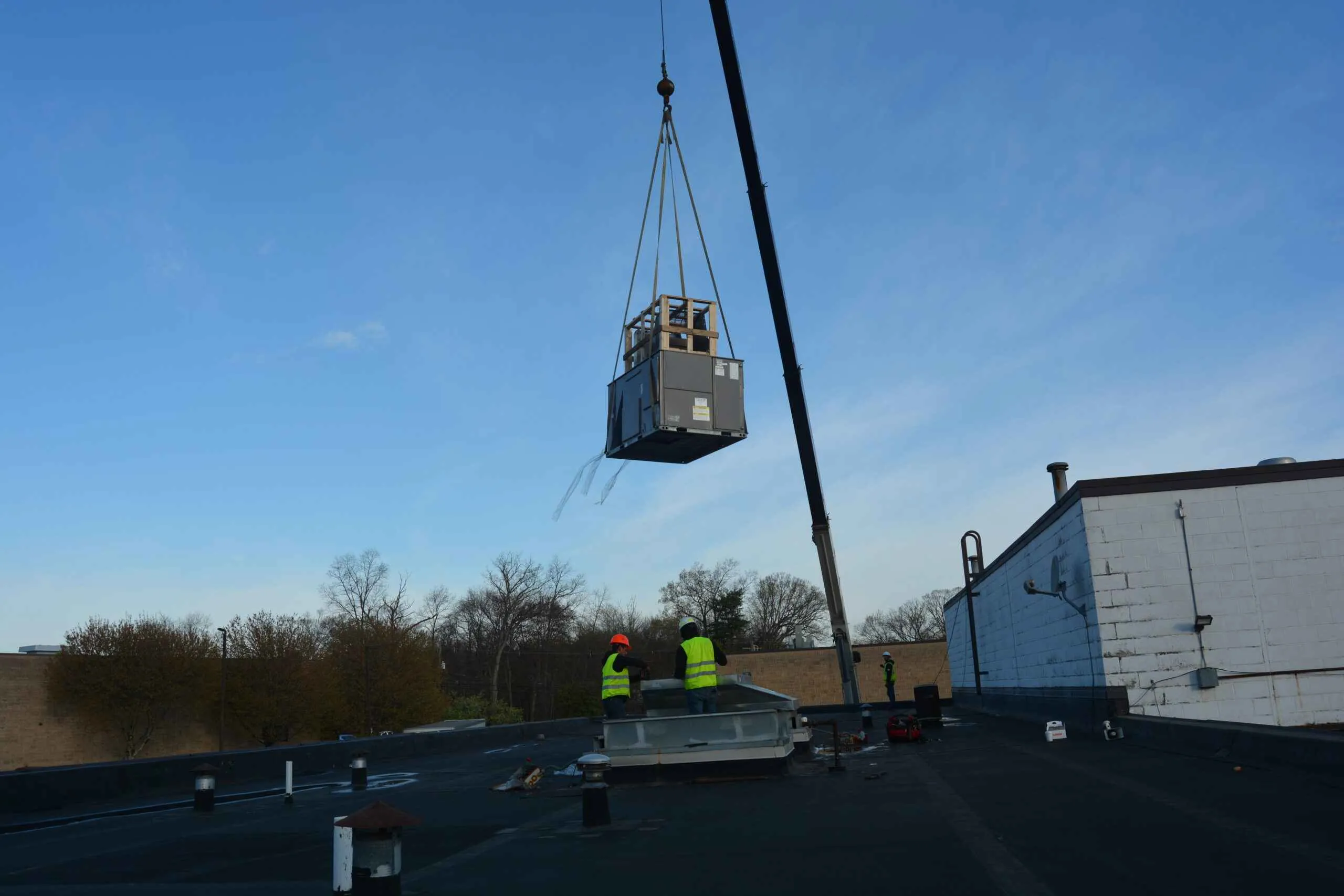 Crane lifting a rooftop HVAC unit into place on a commercial roof